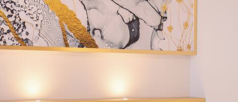 A modern hotel room with a large abstract painting, a bedside table with a lamp, and a headboard.