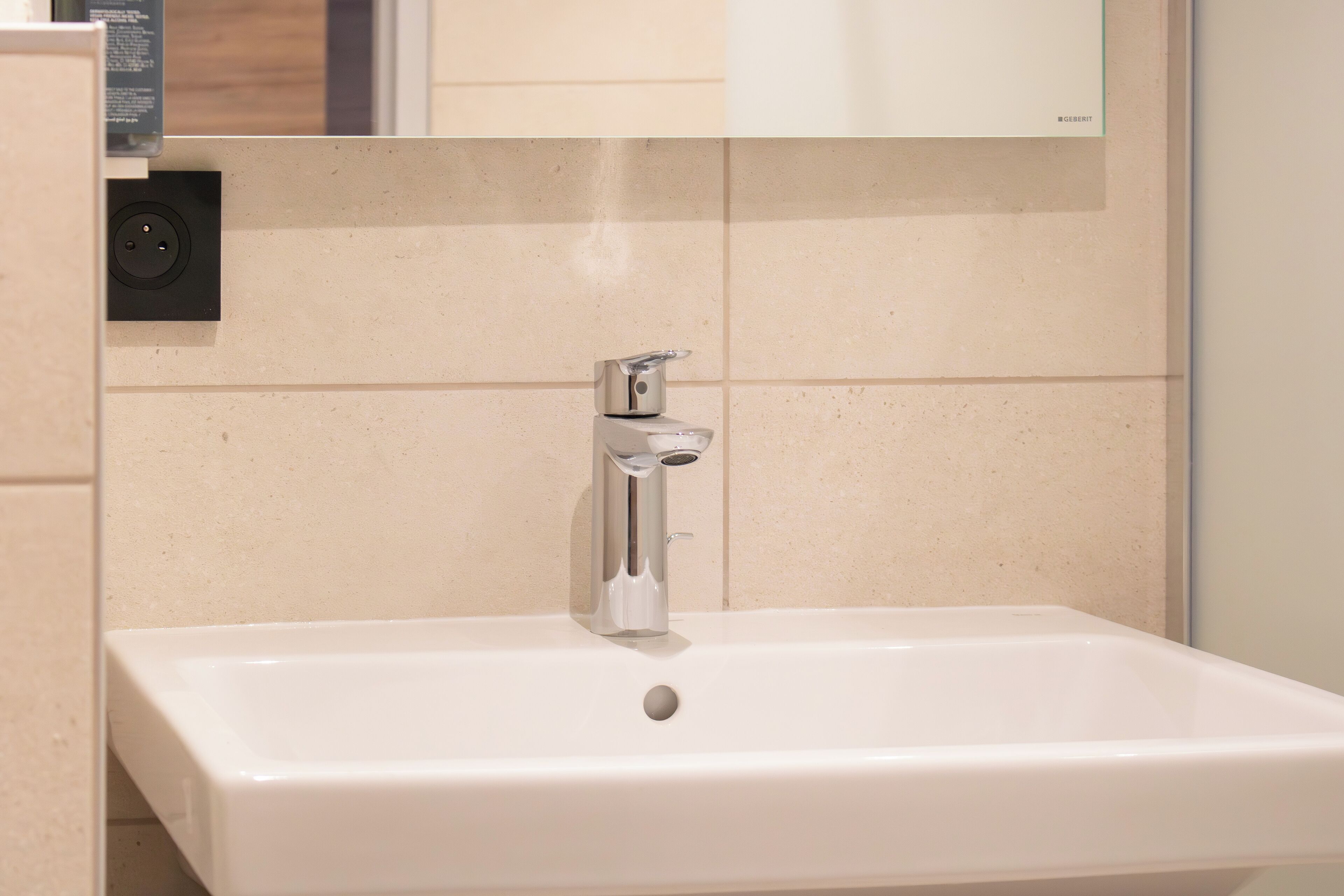A bathroom with a white sink, a mirror above it, and a wall-mounted electrical outlet.