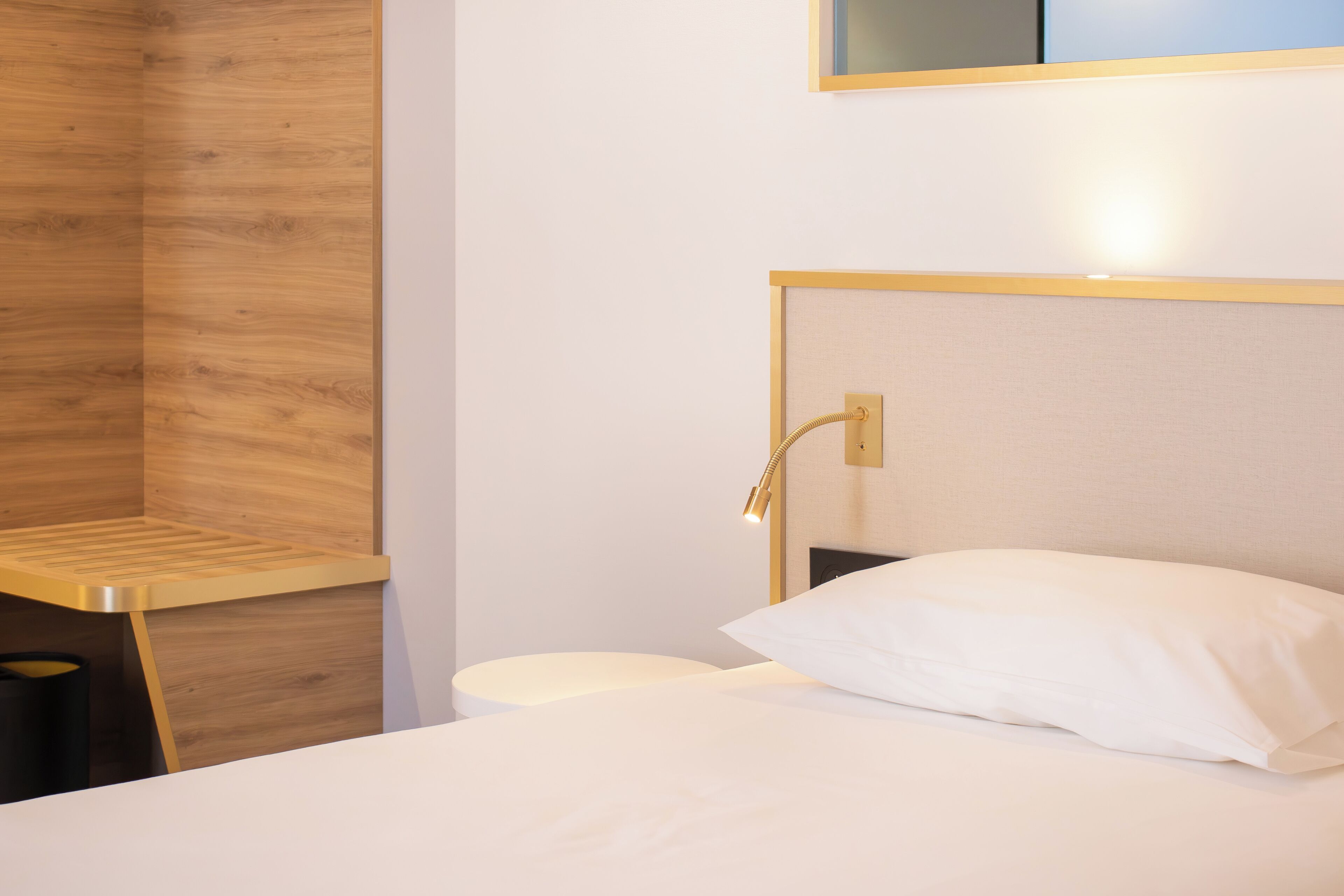 Ein Hotelzimmer mit einer Wand in Holzoptik, einem Bett mit weißer Bettwäsche und einem Nachttisch mit Lampe.