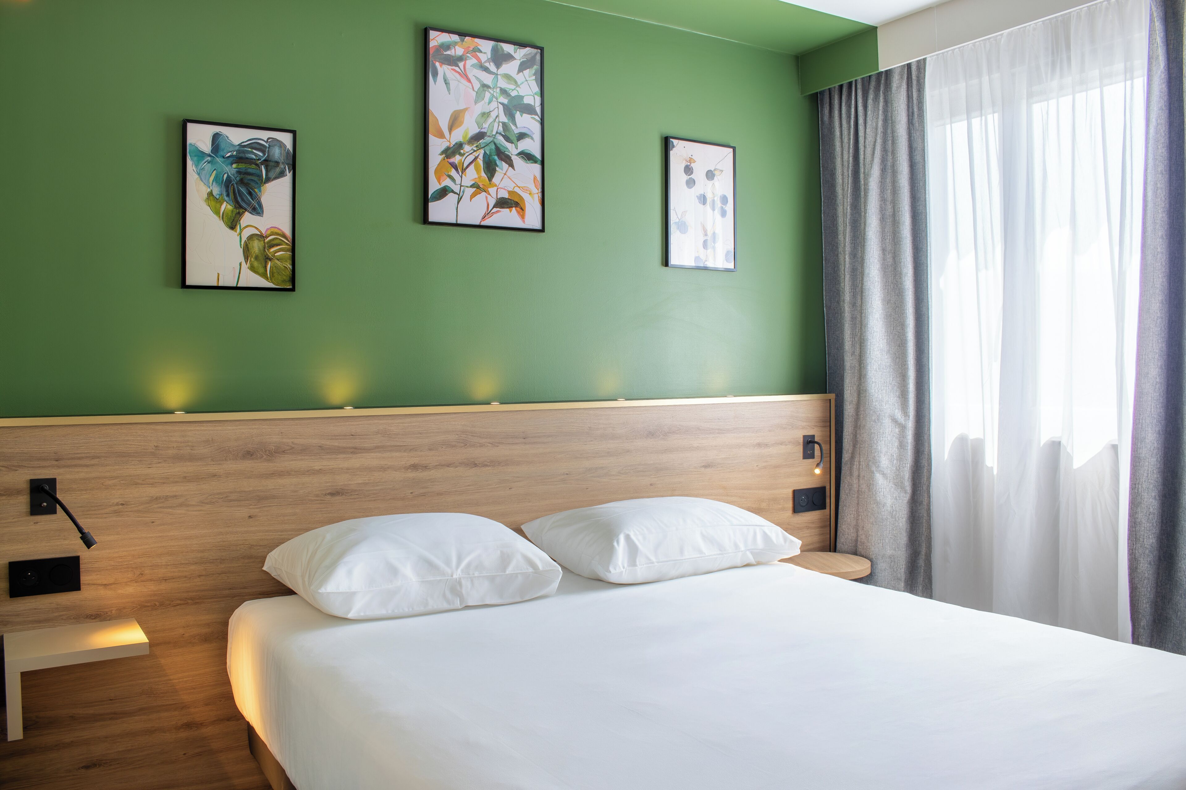 Una habitación de hotel con cabecera de madera, cama con ropa blanca y tres cuadros en la pared.