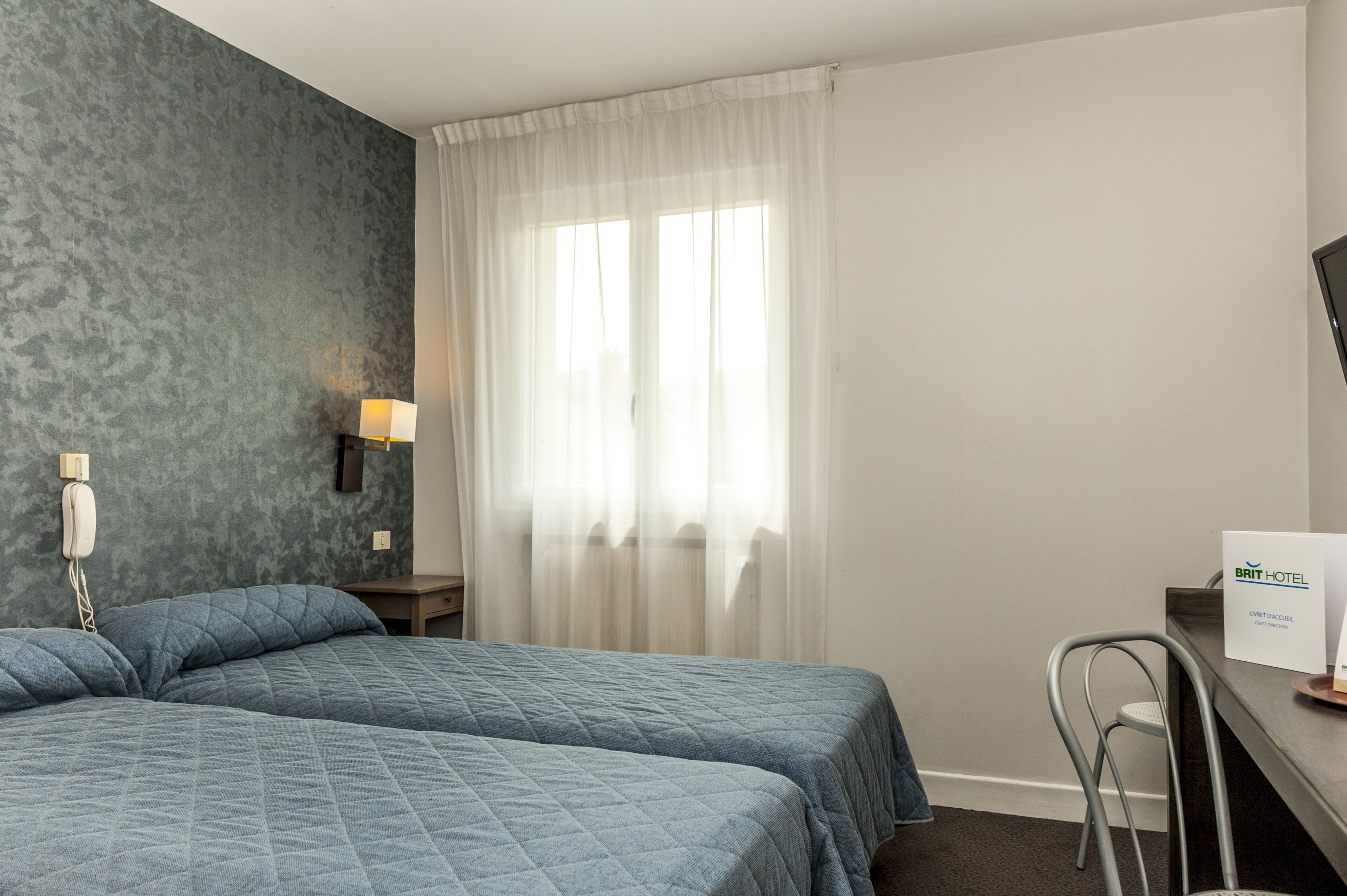 Een hotelkamer met twee bedden, een bureau, een stoel, een lamp en een bordje met het kamertype.