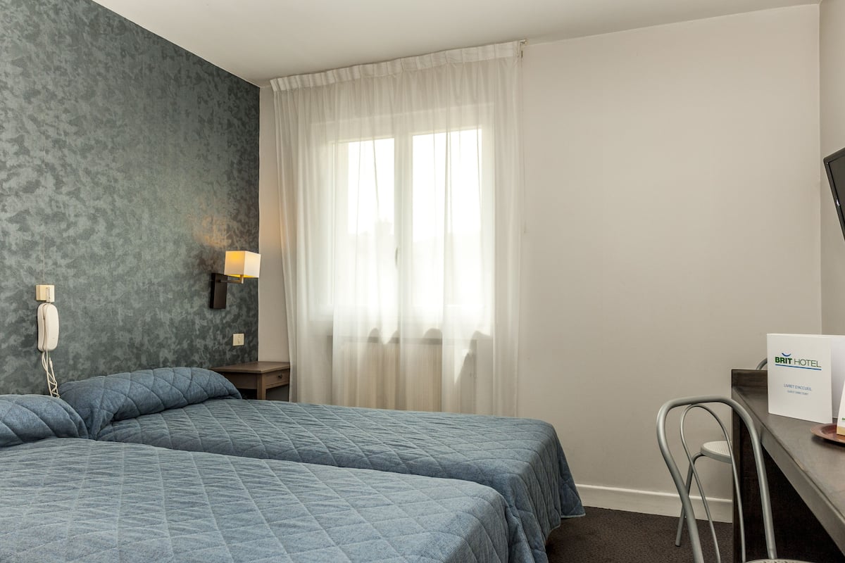 Ein Hotelzimmer mit zwei Betten, einem Schreibtisch, einem Stuhl, einer Lampe und einem Schild, das den Zimmertyp angibt.