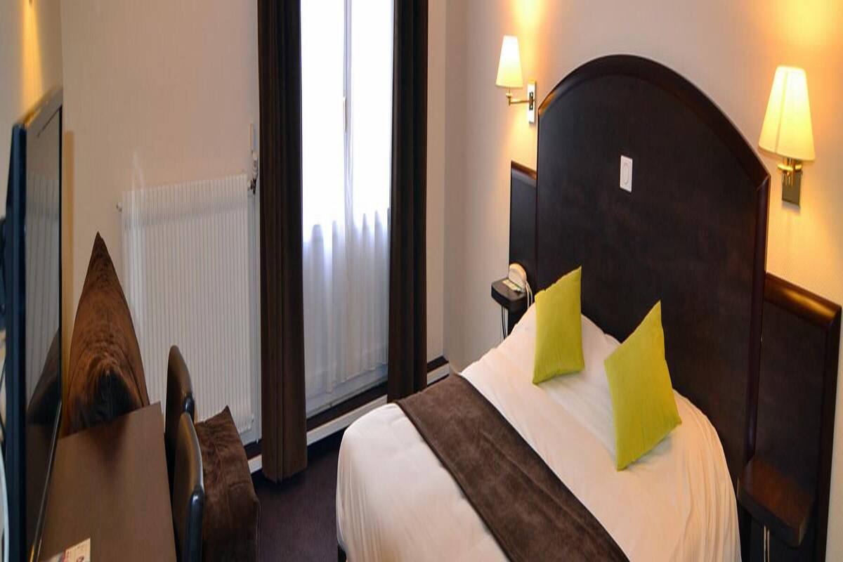 Ein Hotelzimmer mit Bett, Nachttischlampen, einem Fenster mit Vorhängen und einem Heizkörper.