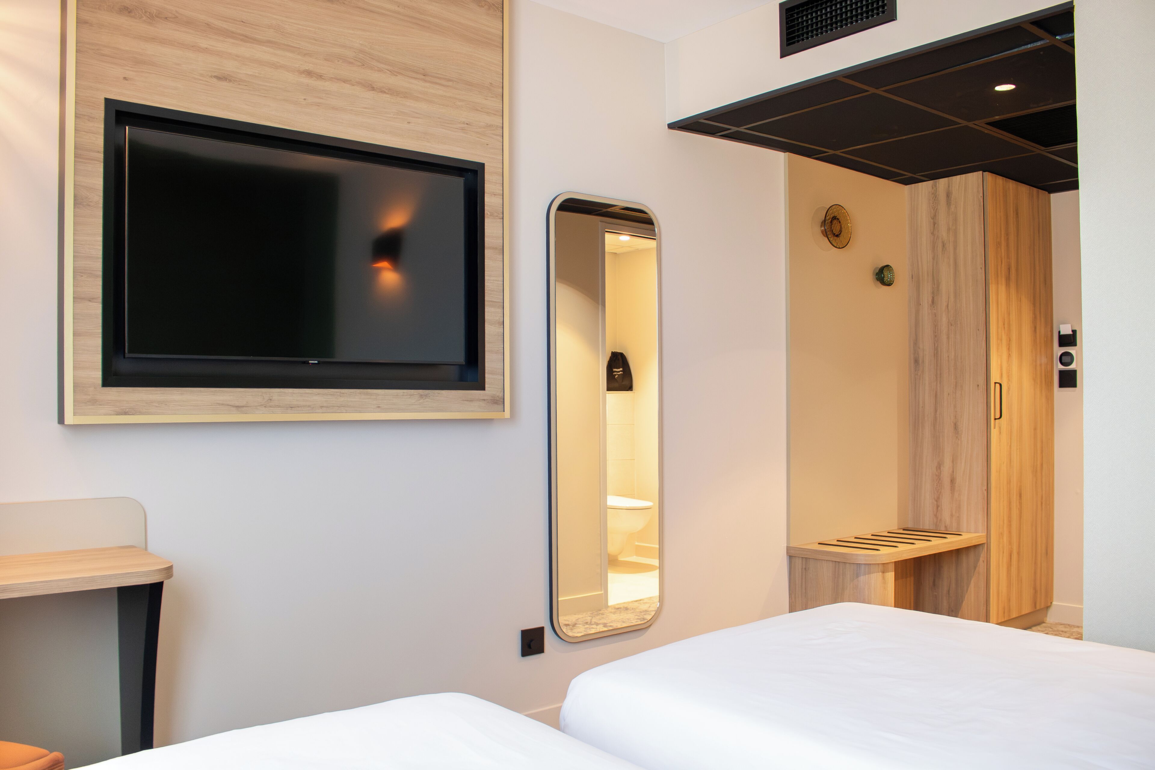 Une chambre d’hôtel équipée d’un lit, d’une télévision, d’un miroir et d’un espace douche.