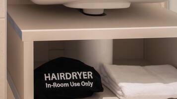 Un baño con un lavabo blanco, un espejo encima y un estante abajo con una gorra negra y una toalla blanca doblada.
