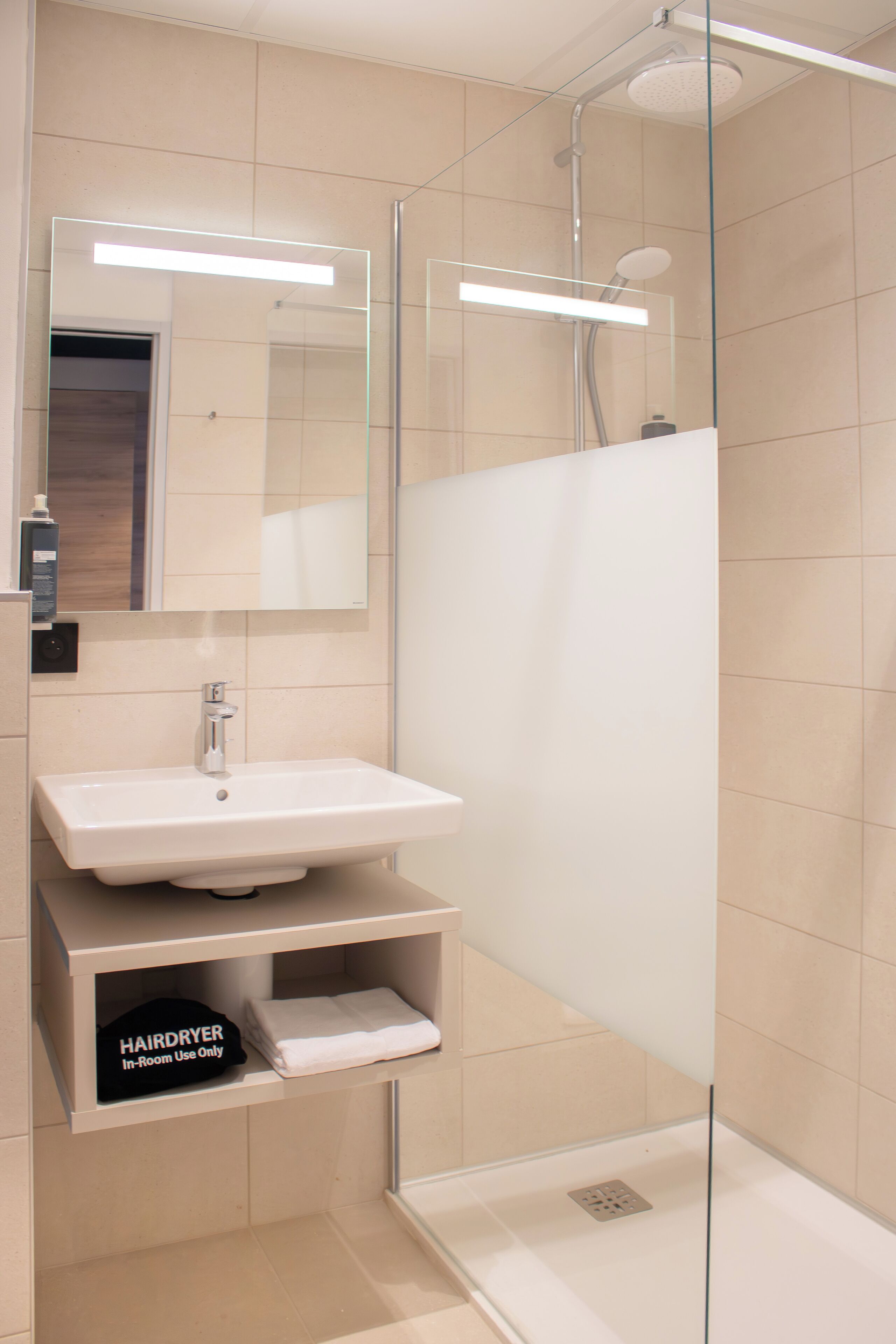 A modern bathroom with a glass-enclosed shower, a white sink, and a mirror above it.