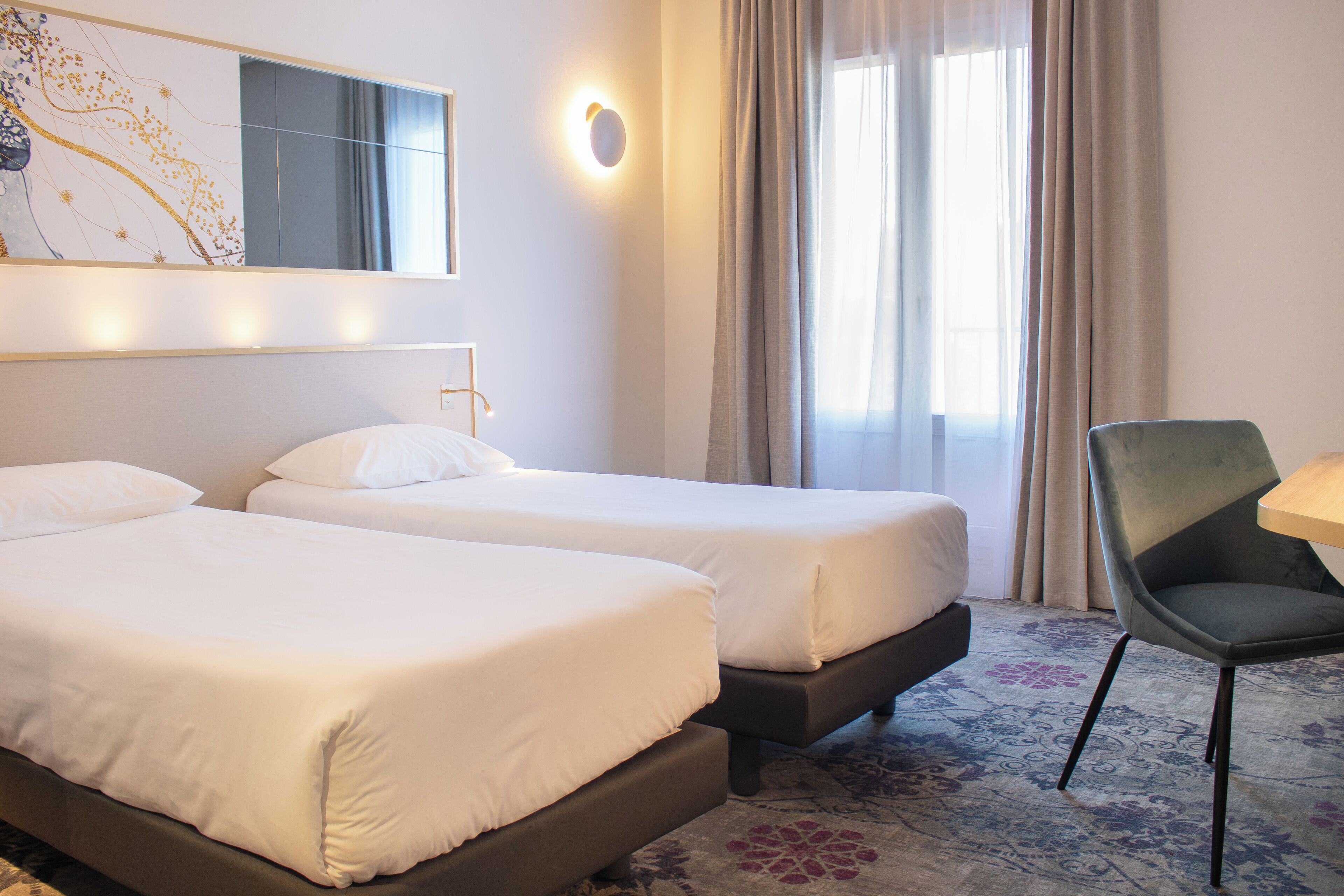 A hotel room with two beds, a chair, a desk, and a large window with curtains.