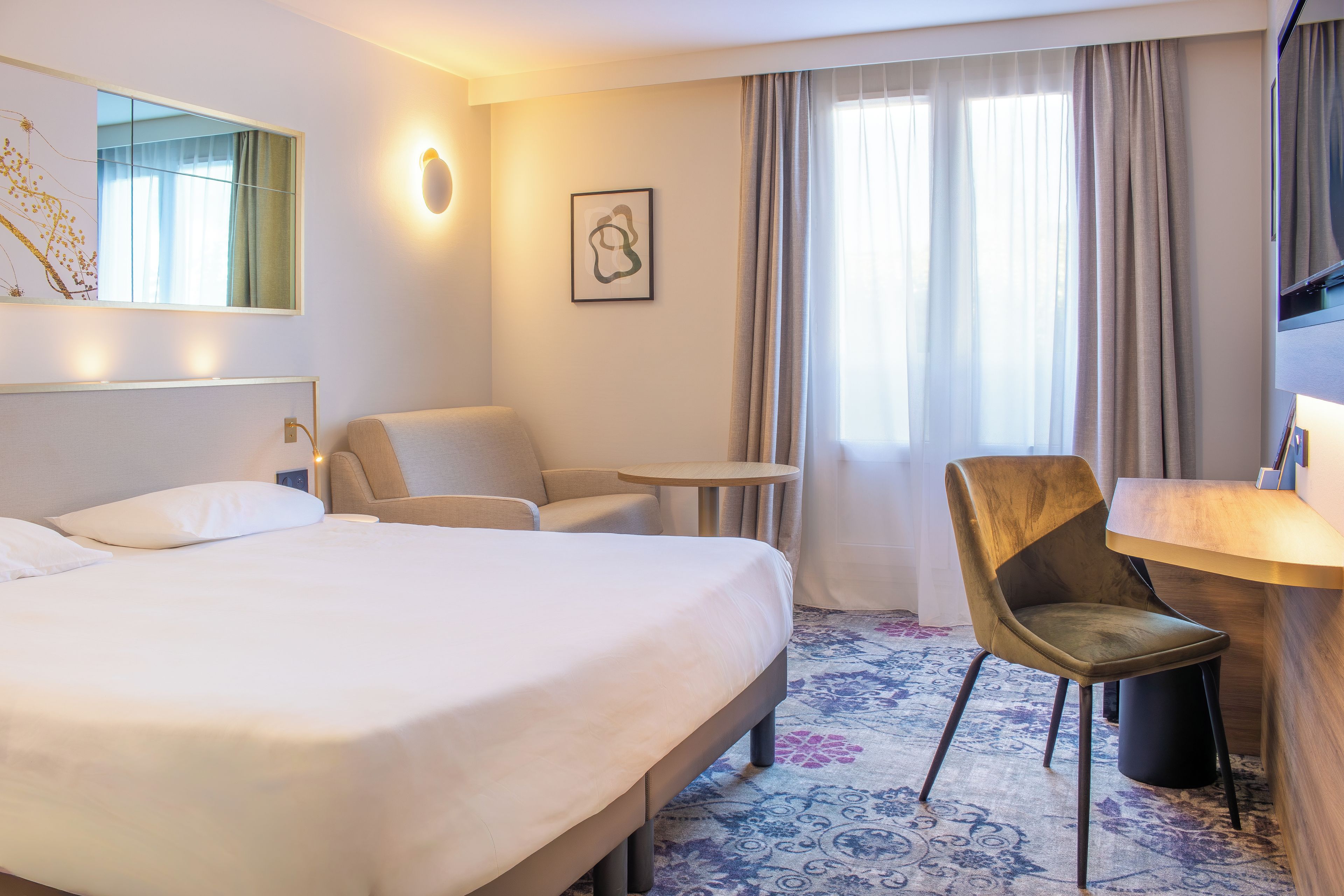 A hotel room with a bed, a desk, a chair, and a TV.