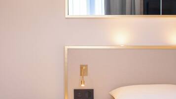 Habitación de hotel con cama, una mesita redonda, una lámpara de pared y un espejo que refleja una ventana con cortinas.