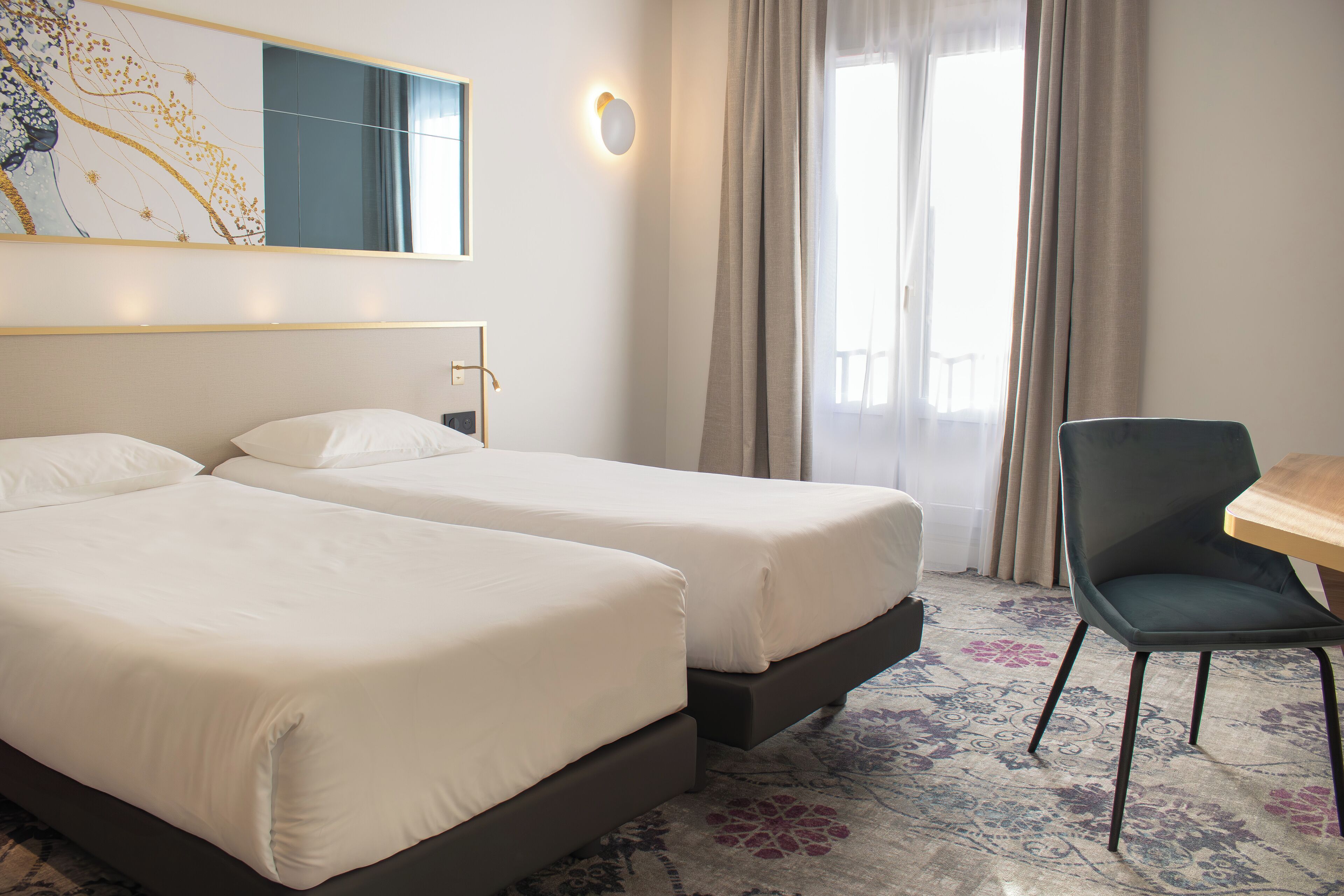 Habitación de hotel con dos camas individuales, un escritorio, una silla y un ventanal con cortinas.