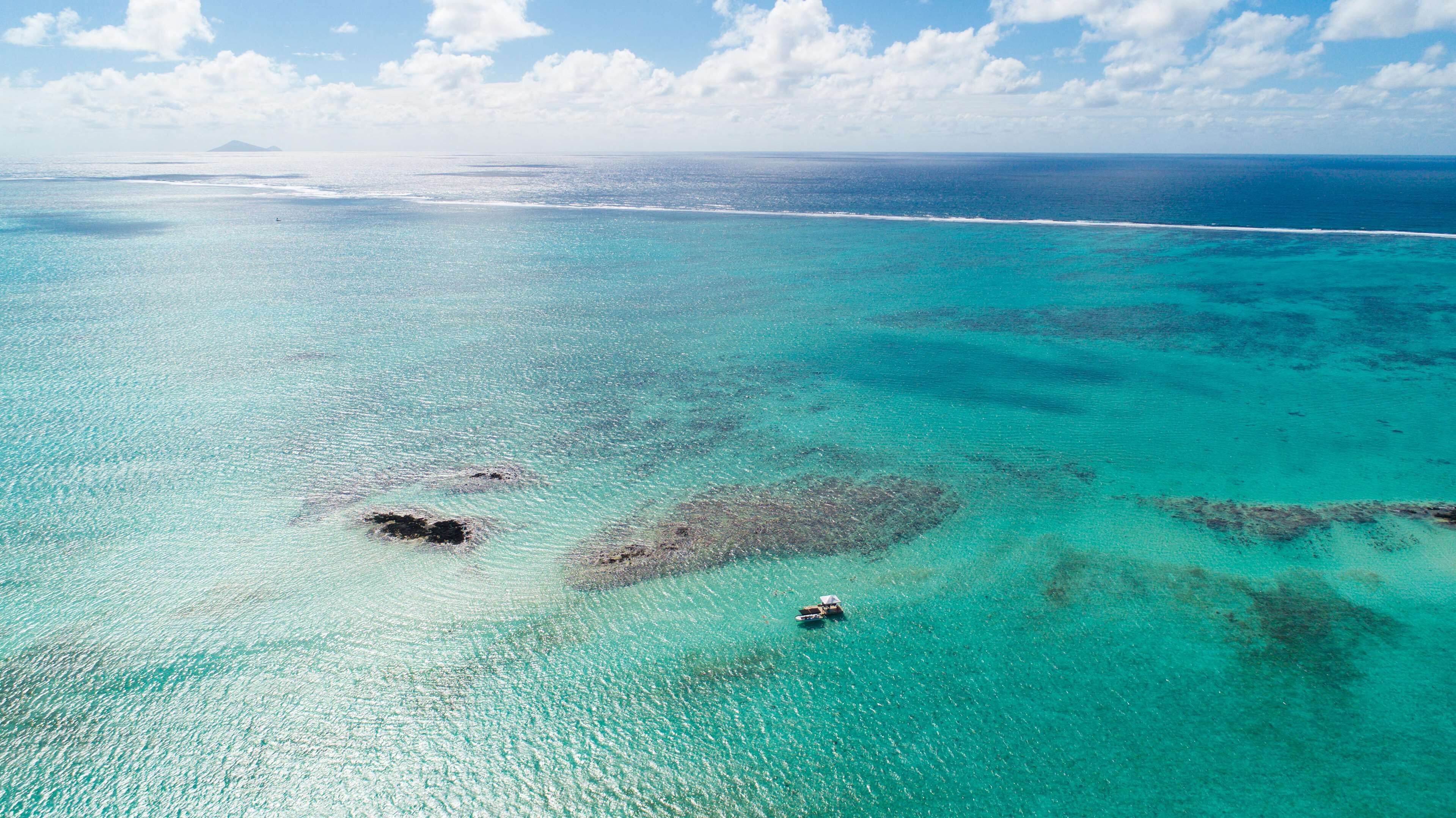 An aerial view of a turquoise sea with clear waters and visible coral formations.