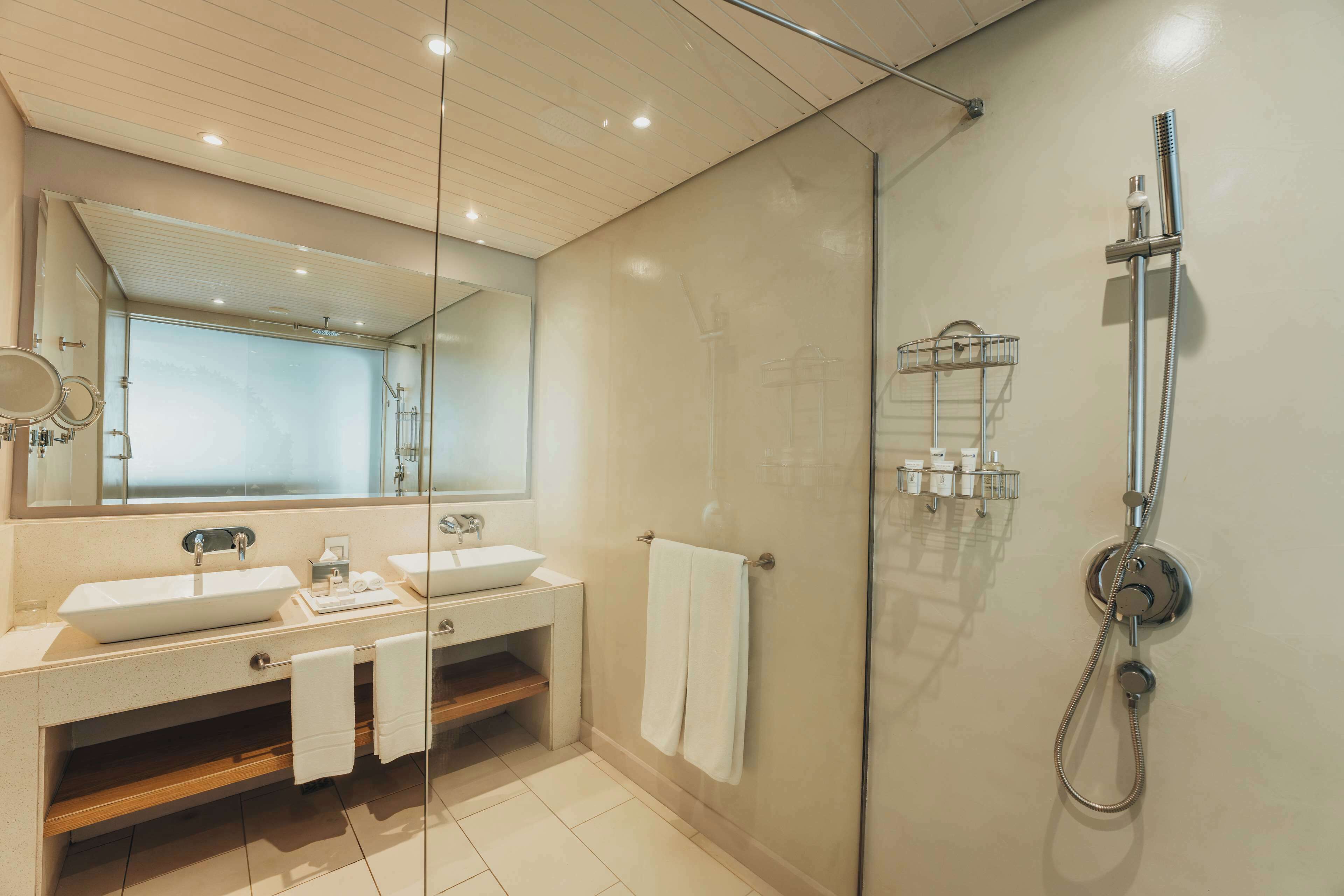 Une salle de bain moderne avec deux lavabos, une douche à l’italienne en verre et un grand miroir.