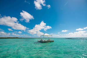 Una plataforma flotante con toldo, rodeada de agua turquesa cristalina y una costa lejana.