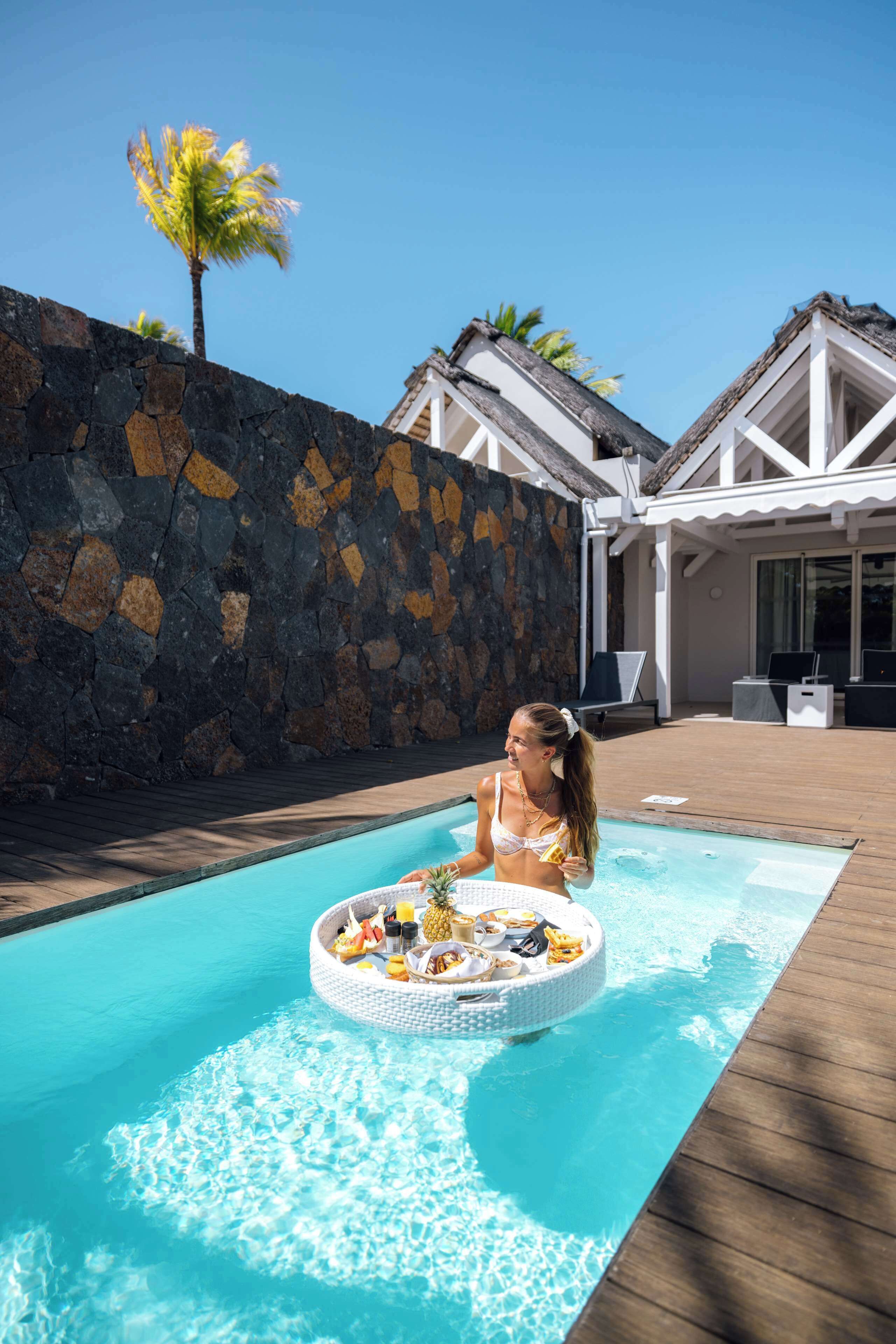 Una piscina con barra flotante, pared de piedra y sillas de descanso.
