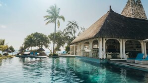 Zona de piscina con sillas de descanso, una estructura de techo de paja y vista al océano.