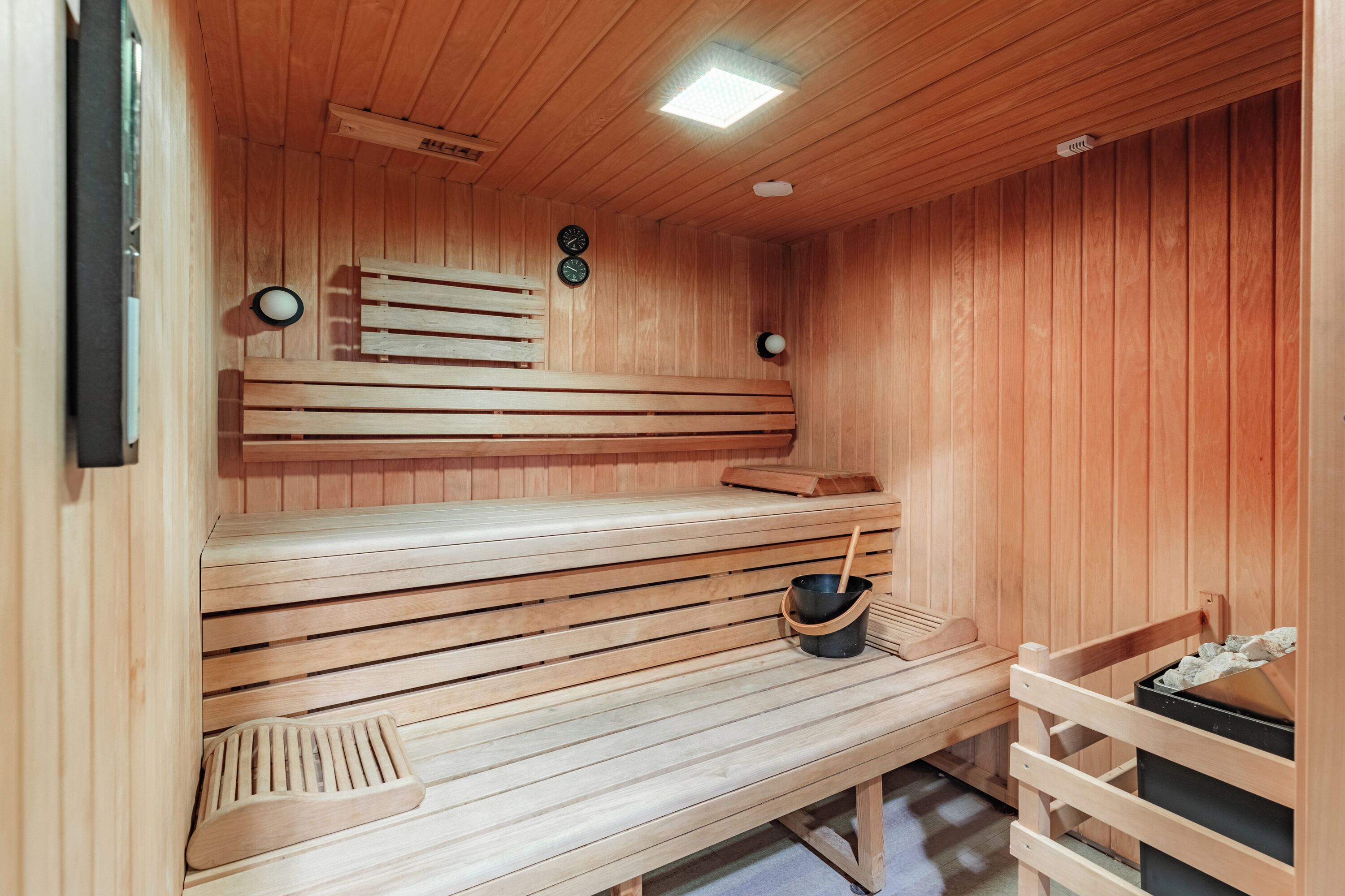 A wooden sauna with benches and a bucket of stones.