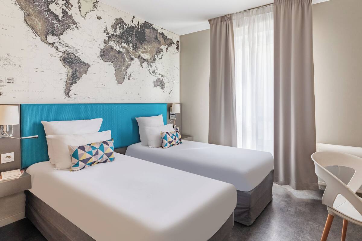 Een hotelkamer met twee bedden, een wereldkaart aan de muur, een bureau met een lamp en een stoel.