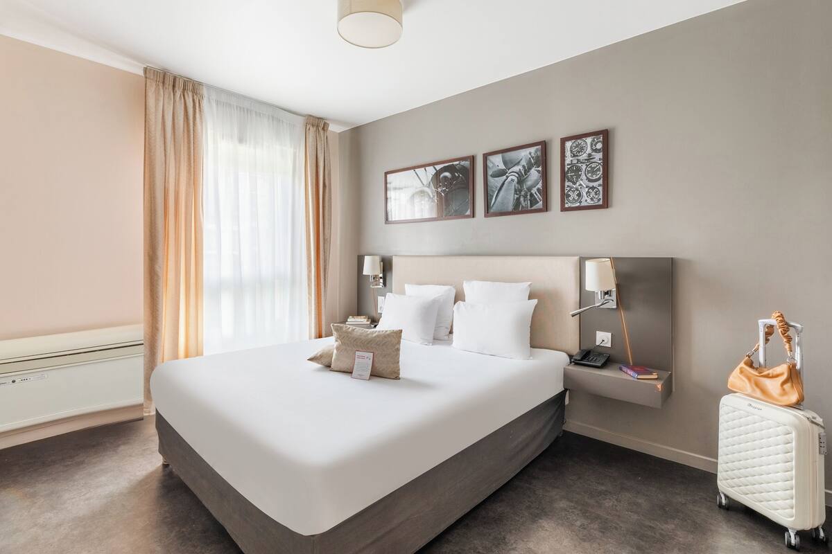 Een hotelkamer met een groot bed, een nachtkastje met een lamp, een koffer en kunst aan de muur.