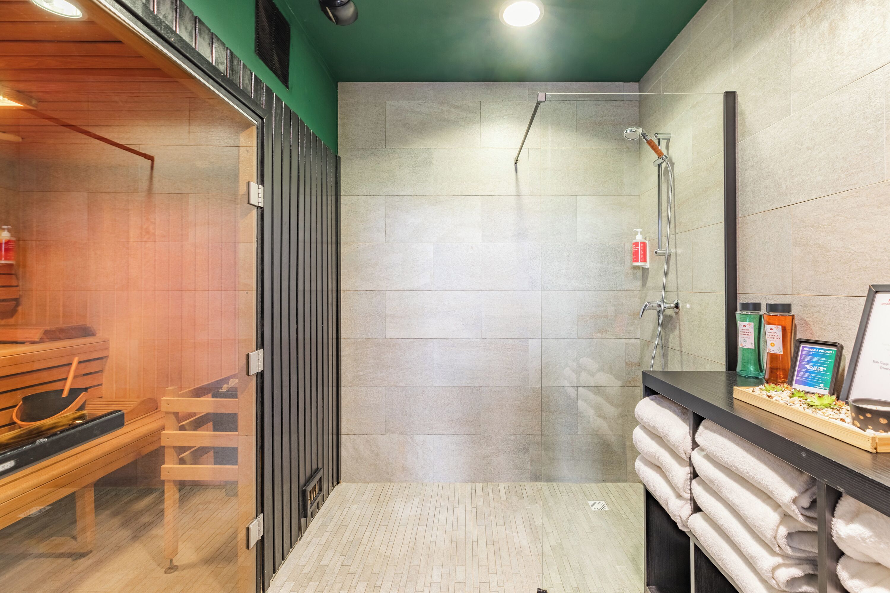Un baño moderno con cabina de ducha de vidrio, banco de madera y toallas ordenadas.