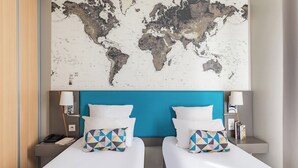 Une chambre d’hôtel avec deux lits, une carte du monde accrochée au mur et une tête de lit bleue.