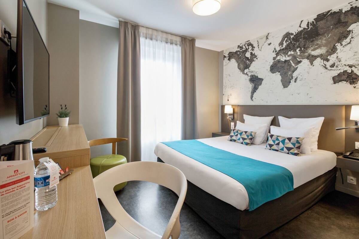 Hotelkamer met een bed, een bureau, een stoel, een televisie en een wereldkaart aan de muur.