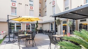 Un espace extérieur aménagé en terrasse, avec des tables et des chaises, un parasol jaune et des plantes en pot.