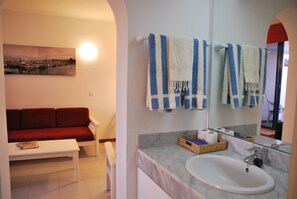A bathroom with a sink, mirror, towels, and a red couch in the adjacent living area.