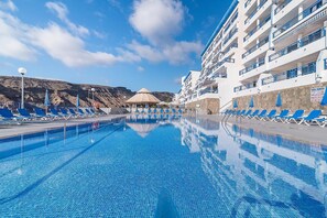 A swimming pool with lounge chairs and a building with balconies.