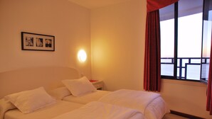 A hotel room with two beds, a nightstand, a framed photo on the wall, and a window with curtains. - HV Apartamentos Vista Taurito (Mogan)