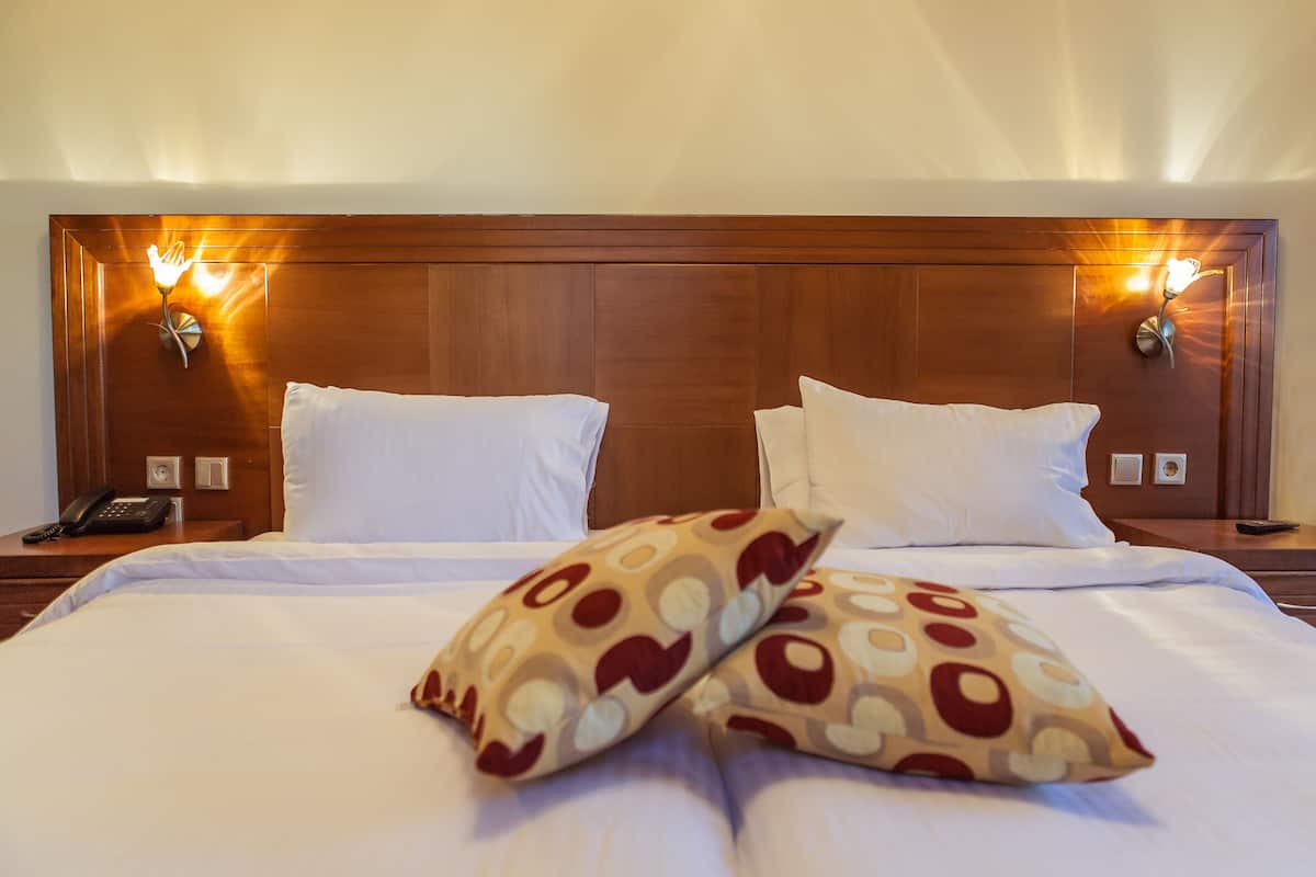 A hotel room with a wooden headboard, two bedside lamps, a telephone, and patterned pillows.