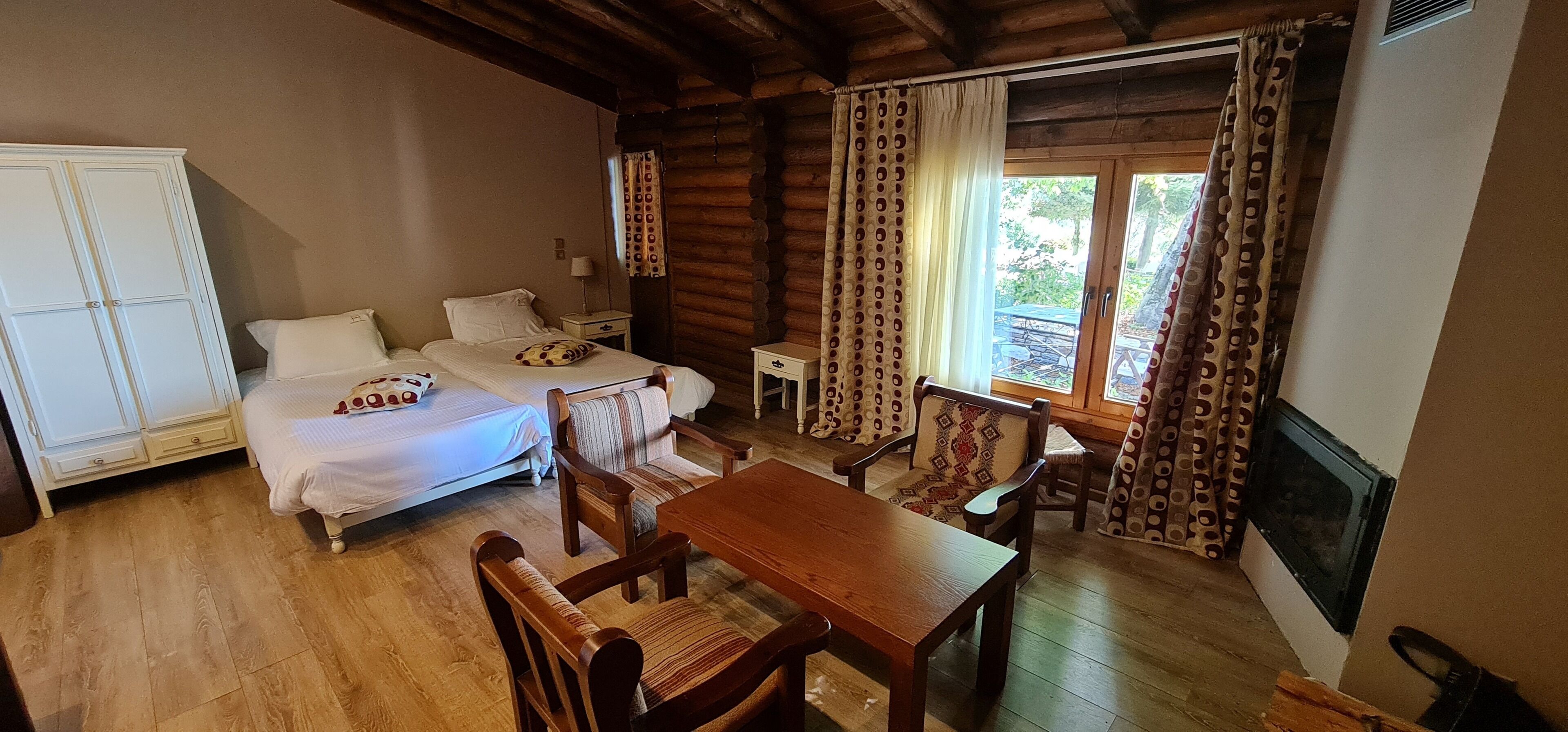 A cozy room with a bed, two chairs, a wooden table, and a TV.