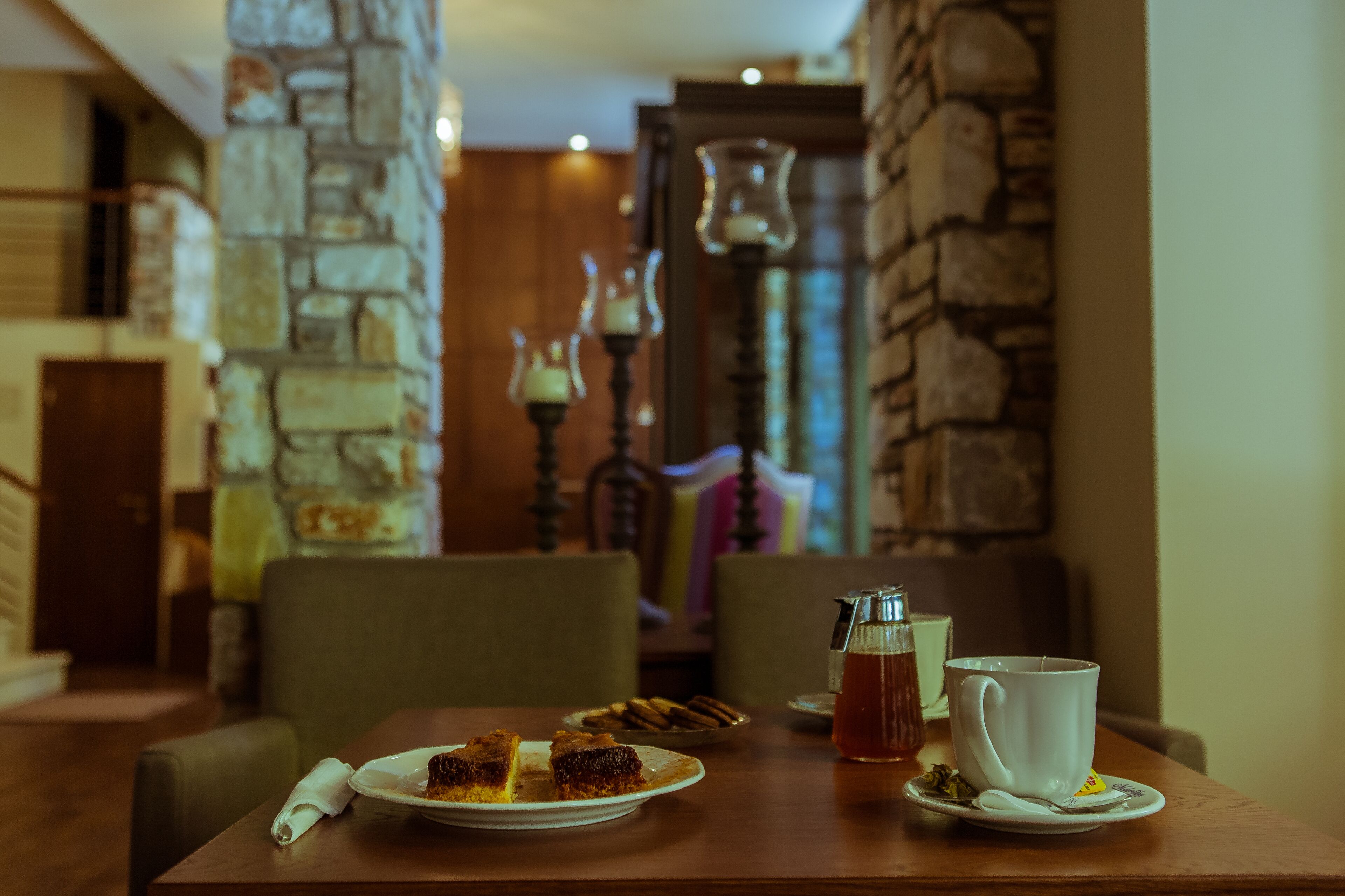 Una mesa de comedor con un plato de comida, una taza de té y una tetera. La habitación tiene paredes de piedra y techo de madera.