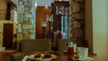 A dining table with a plate of food, a cup of tea, and a teapot. The room has stone walls and a wooden ceiling.