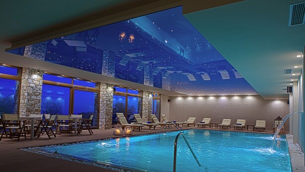 An indoor swimming pool with a night sky mural, stone walls, and lounge chairs.