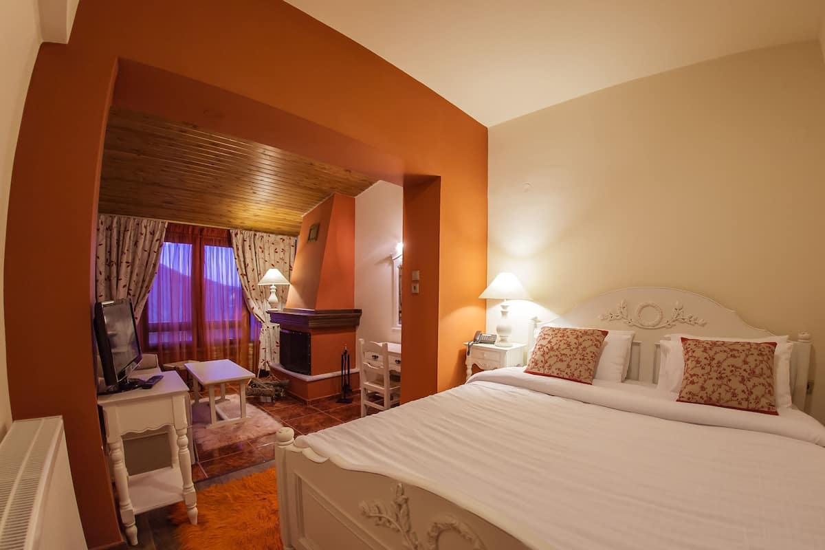 A hotel room with a bed, a desk, a chair, a television, and a fireplace.