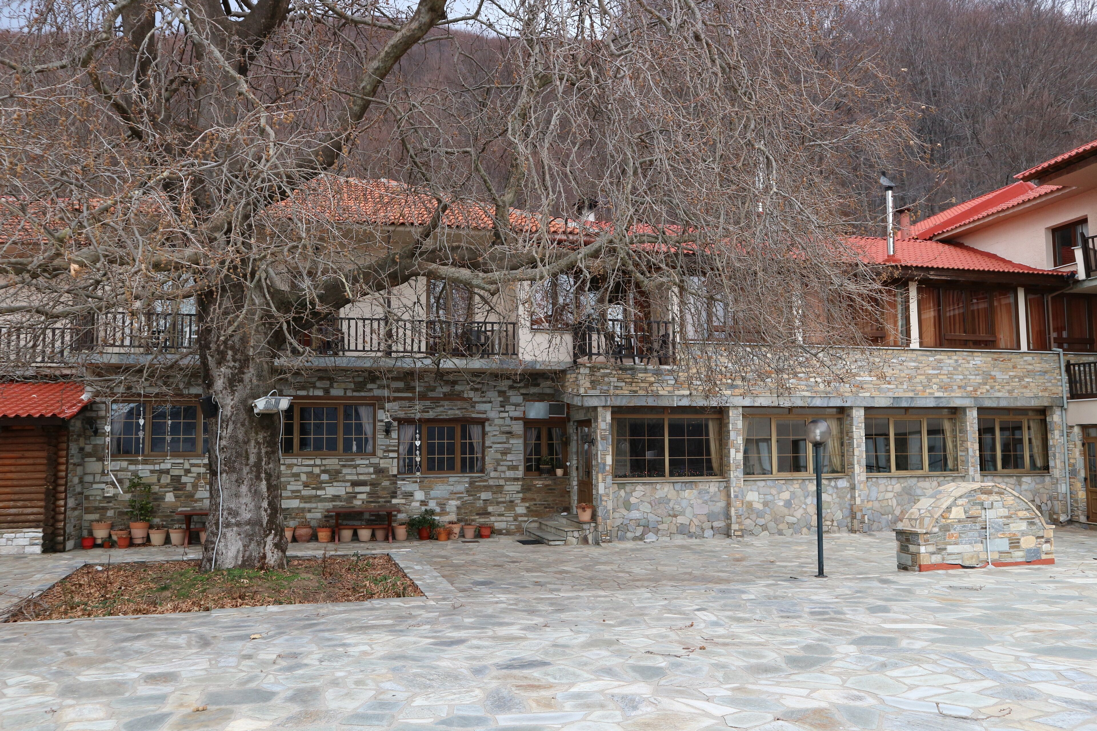 A stone building with a red roof, a stone archway, and a tree in the courtyard.