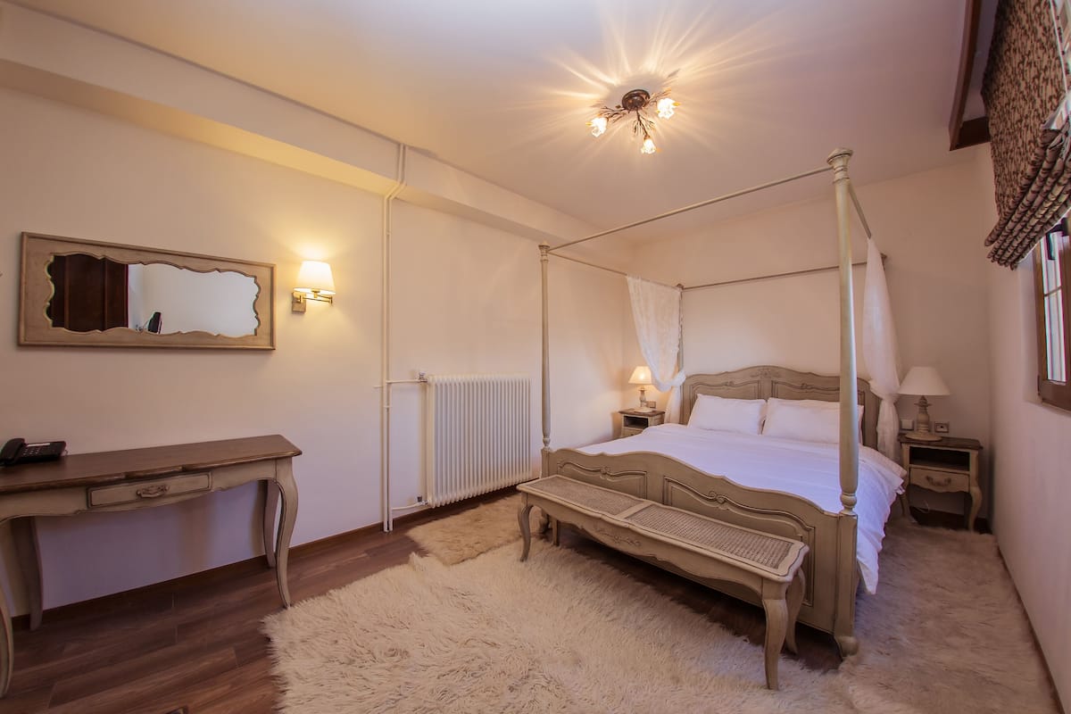 A four-poster bed with a canopy, a bedside table with a lamp, a wooden desk with a telephone, and a large mirror on the wall.