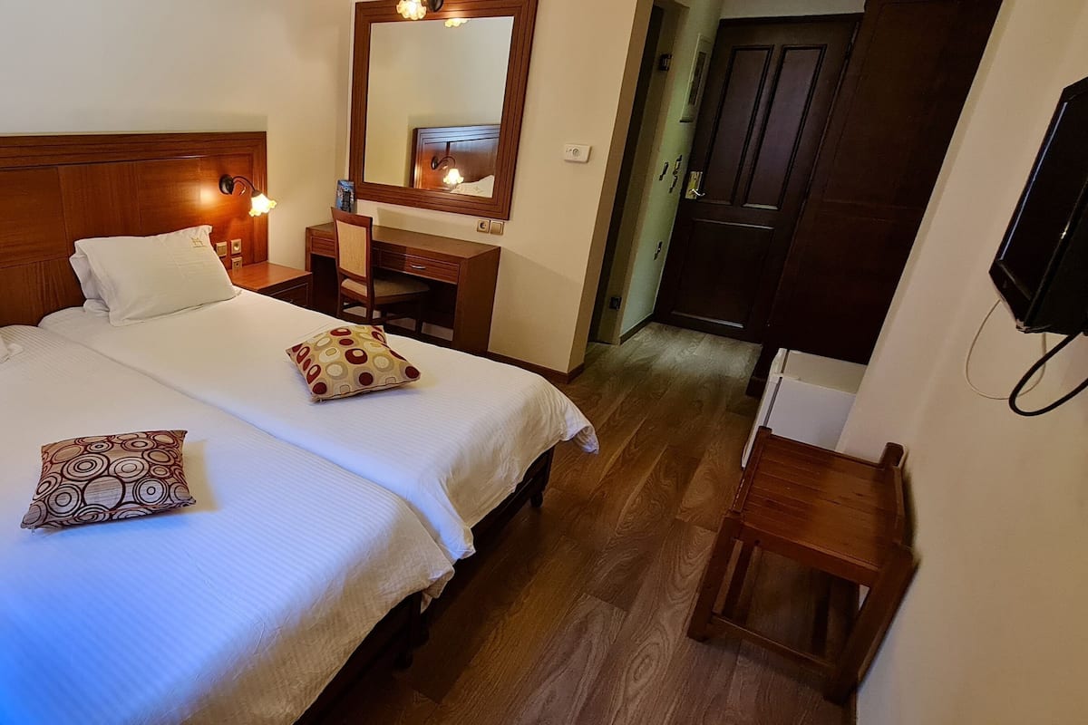 A hotel room with a double bed, bedside lamps, a desk, a chair, a mirror, and a television.