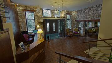 A spacious lobby with a wooden reception desk, stone walls, and a staircase.