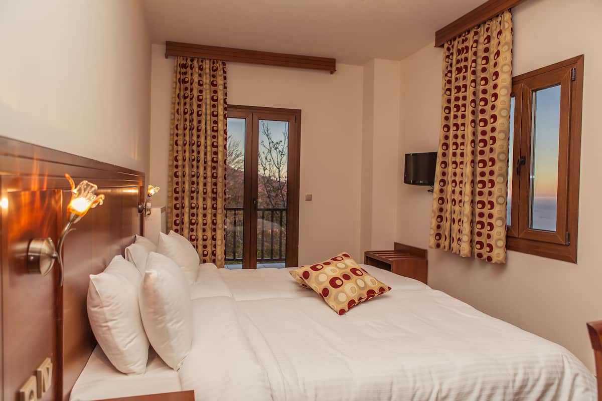 A hotel room with a bed, curtains, a television, and a window.