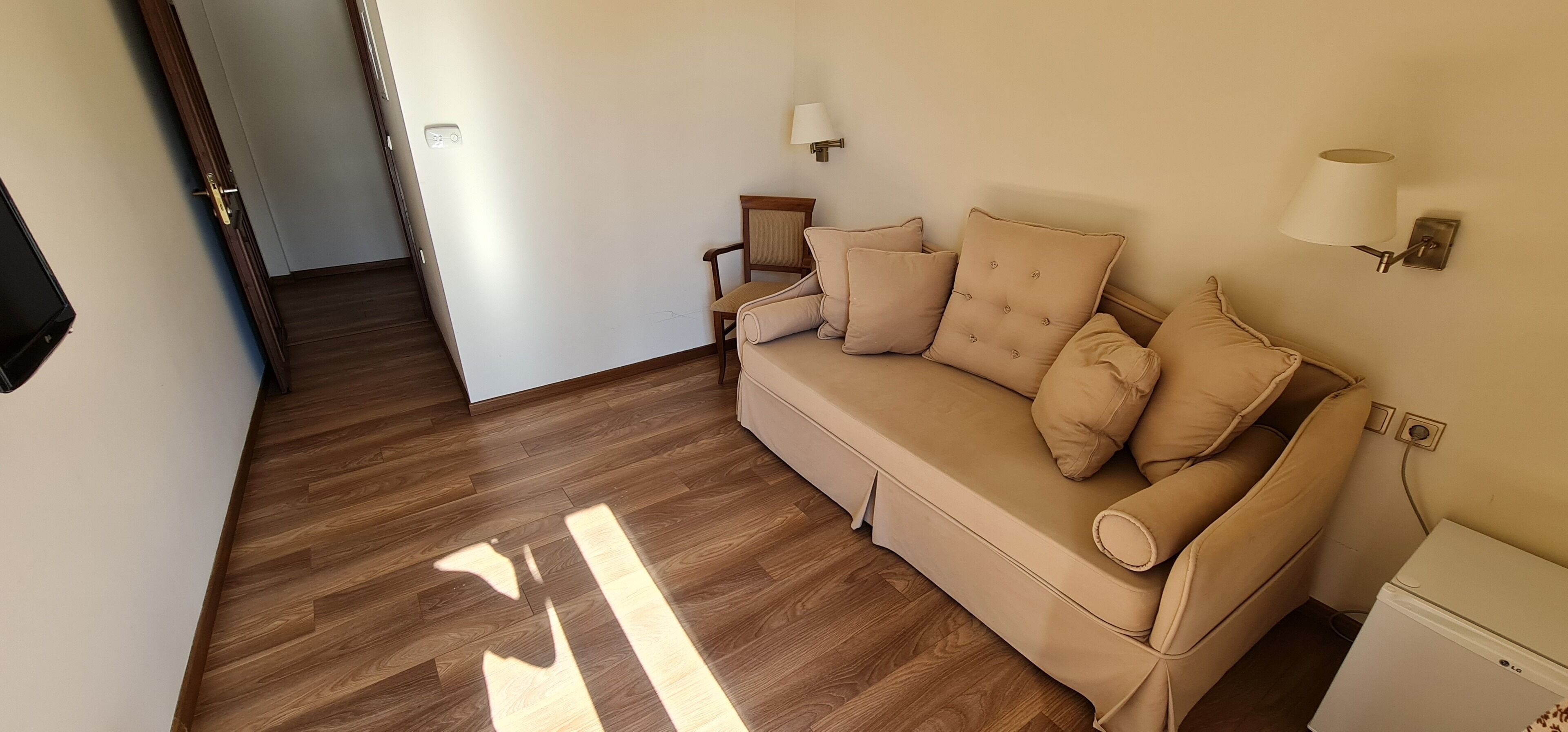 Una habitación con un sofá color beige, dos lámparas de pared y una mesita.