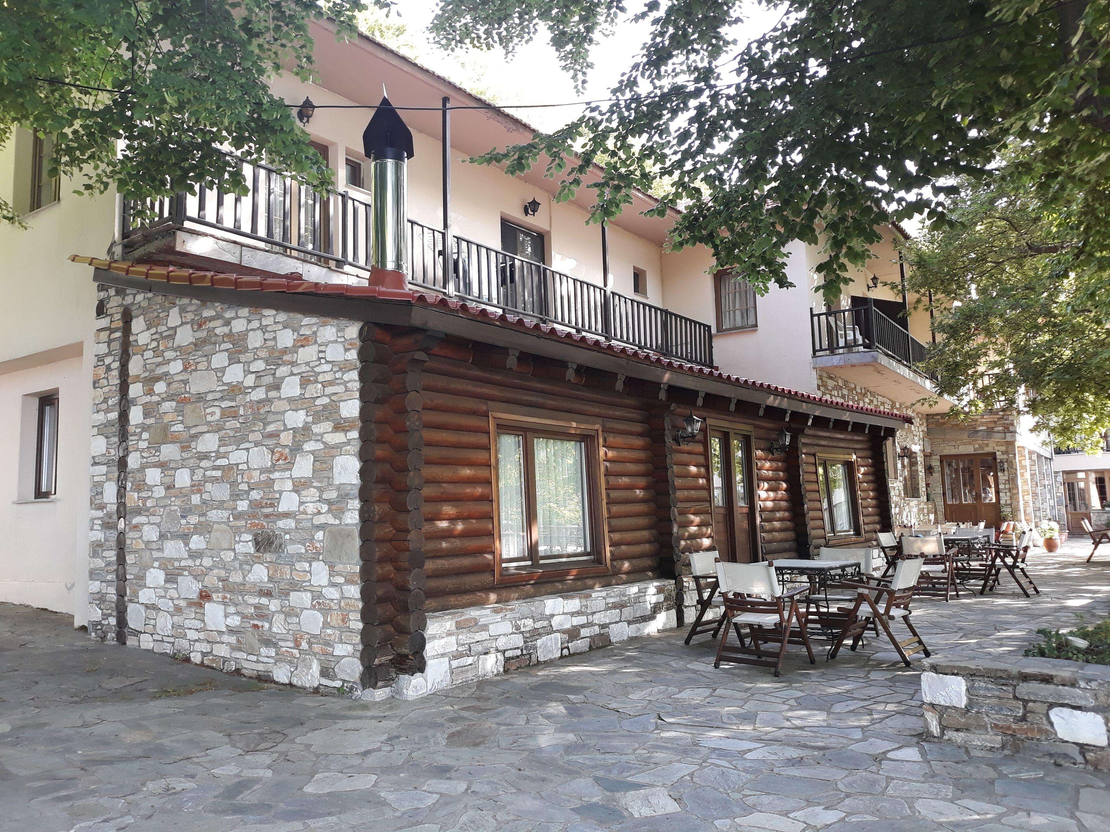 A rustic log cabin with stone walls, a balcony, and outdoor seating.