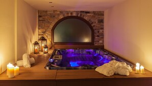 A spa room with a stone wall, a large arched mirror, a hot tub, and candles.