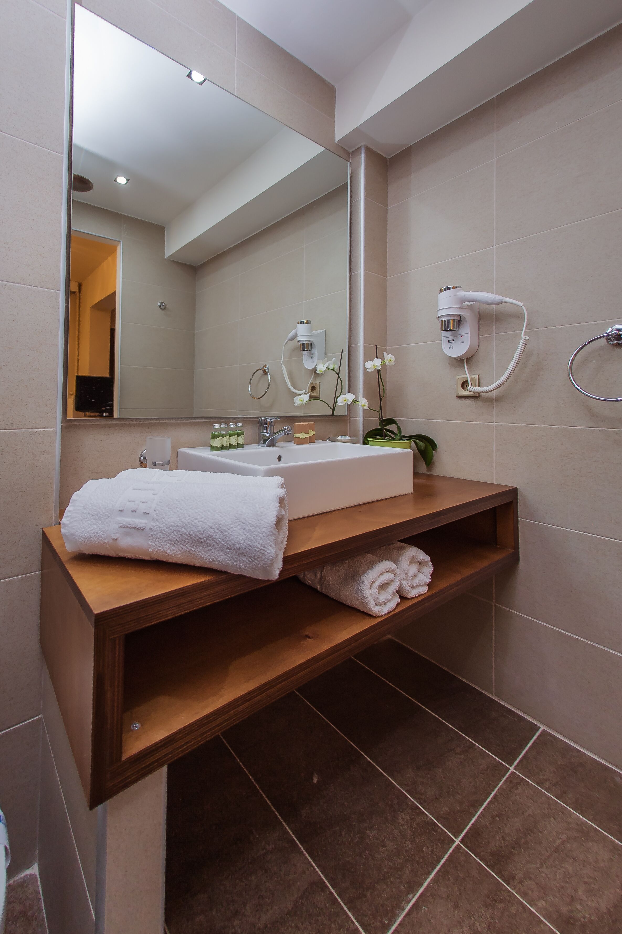 A bathroom with a wooden vanity, a white sink, a mirror, a towel rack, and a shower area.