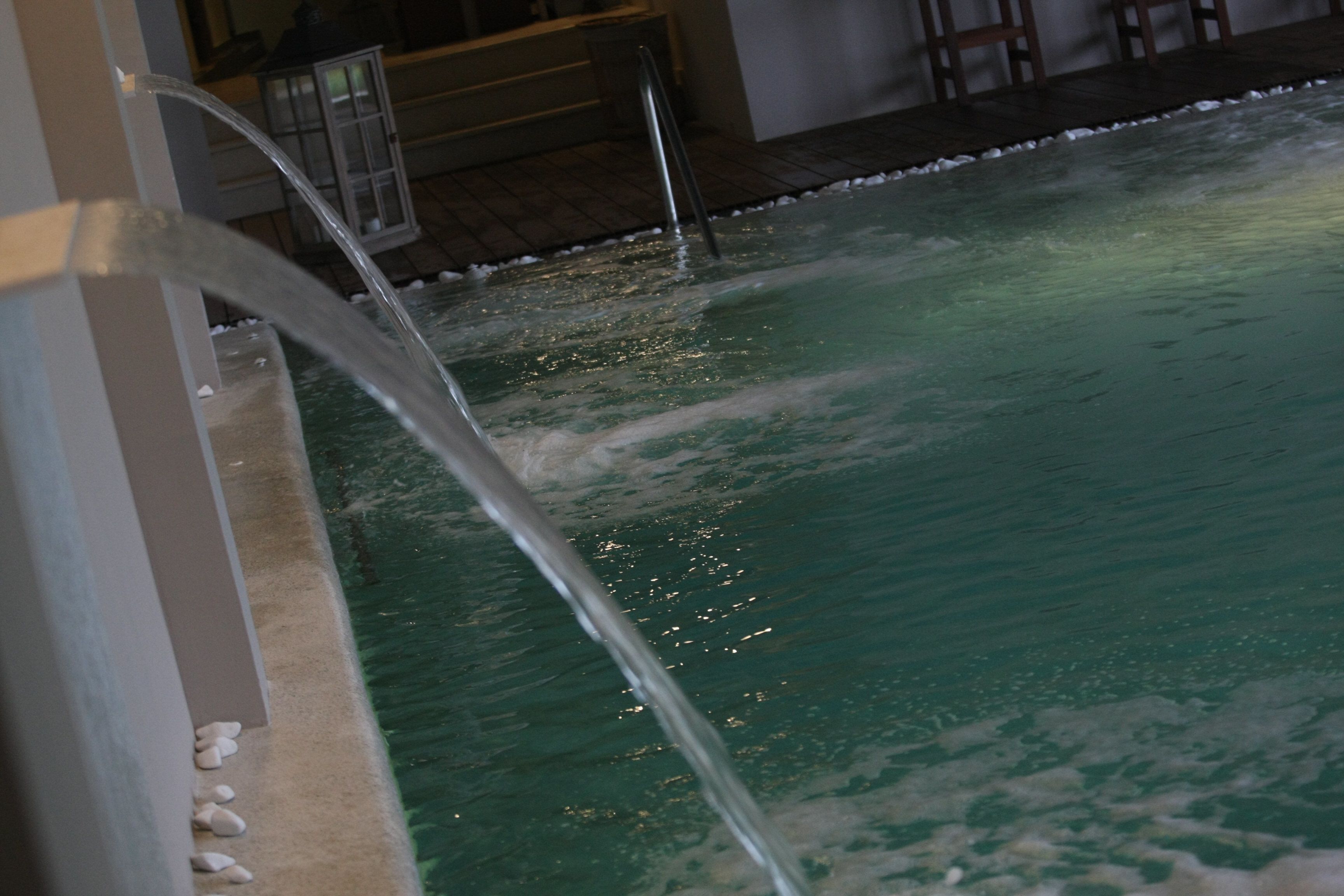 A pool with clear water, a metal ladder, and a tiled floor.
