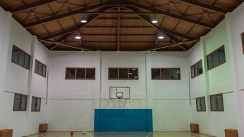 Een binnentoekomstzaal met basketbalveld, houten plafond, meerdere ramen en een blauwe, beklede muur.