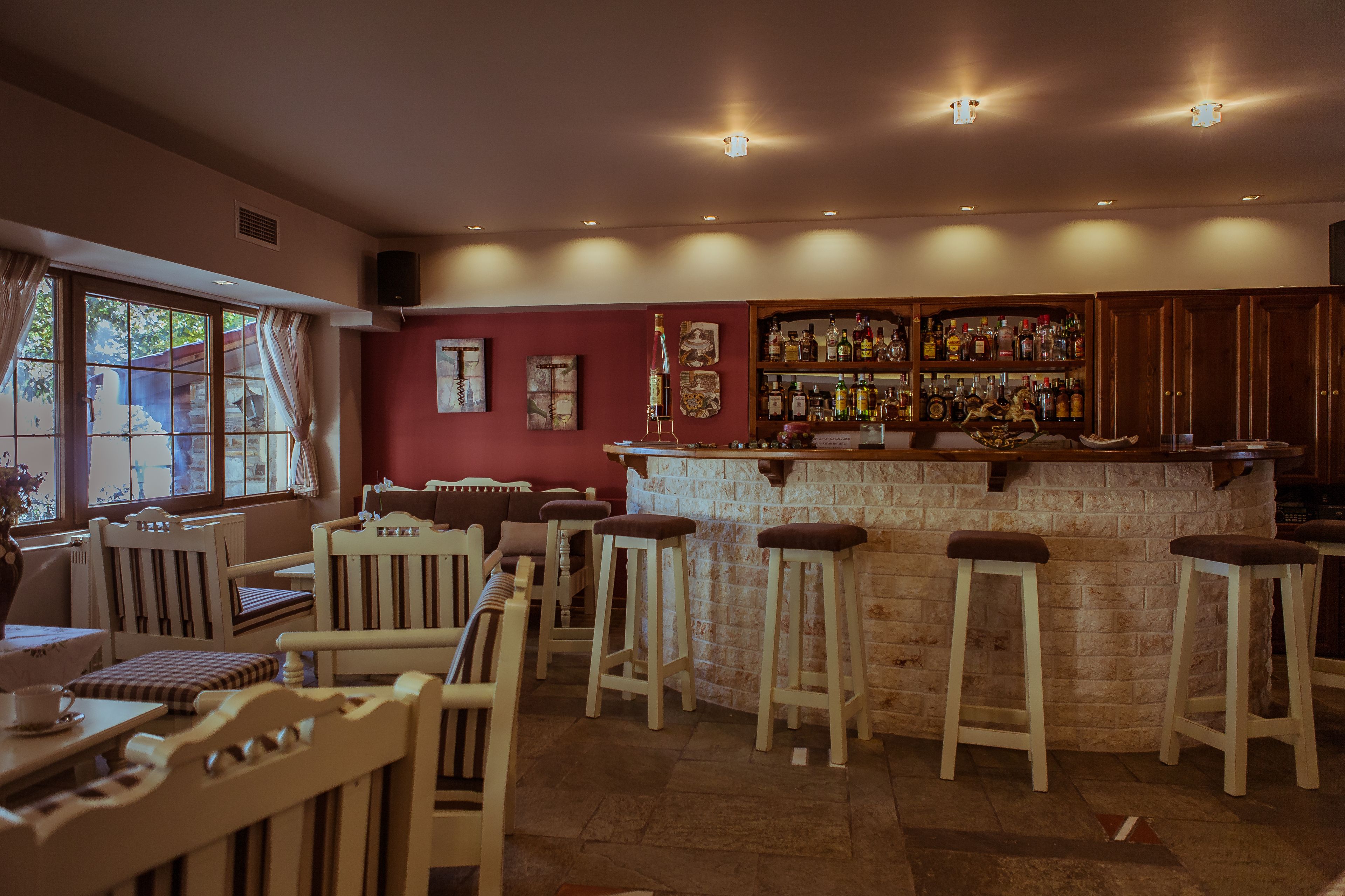 A bar area with wooden stools, a bar counter, and a selection of bottles.