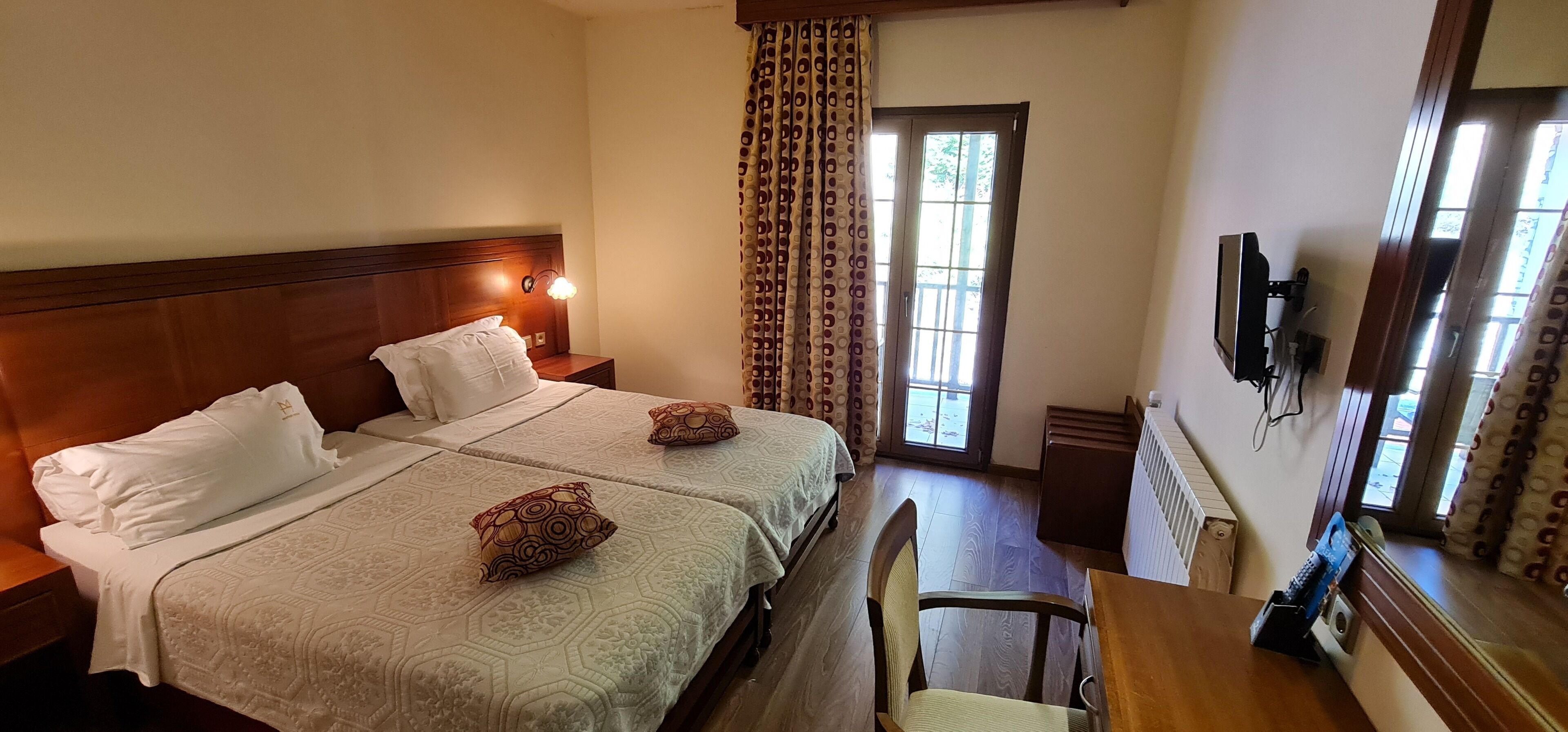 A hotel room with two beds, a desk, a chair, a TV, and a window with curtains.