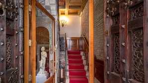 Un magnifique escalier recouvert d’un tapis rouge mène à un palier, de part et d’autre duquel se trouvent des portes en bois richement sculptées.