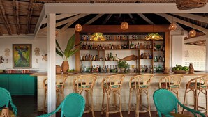A bar area with wicker chairs and a bar counter stocked with bottles. - East Winds Saint Lucia (Gros Islet)